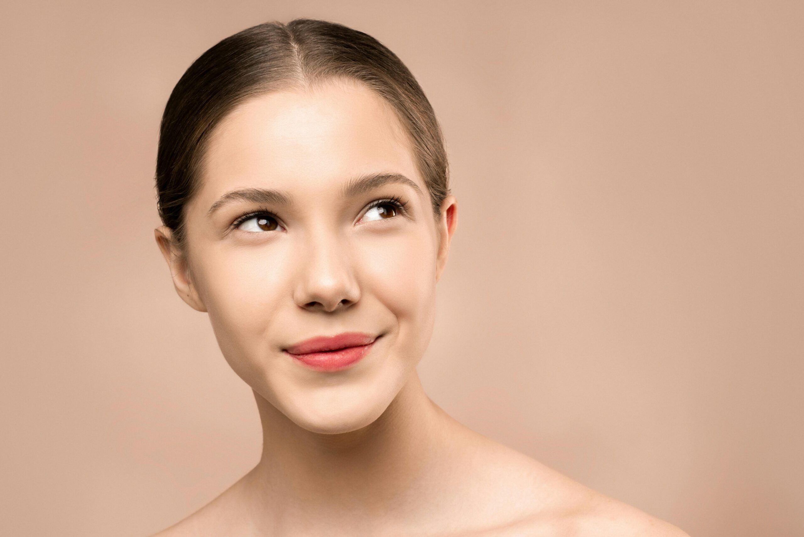 Portrait of a young woman smiling with radiant, flawless skin against a nude background.